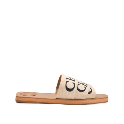 A pair of beige flat sandals with a text pattern on the strap and a simple sole design.
